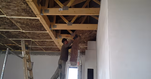 Dachgeschossausbau: Monteur bringt Dämmung zwischen den Holzbalken an
